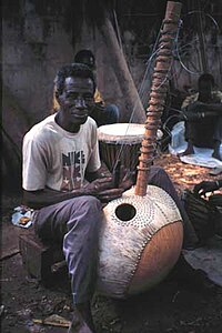 Photographie en couleur d'un homme noir fabriquant à la main un grand instrument de musique à cordes