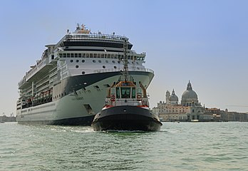 Le Celebrity Summit tiré par un remorqueur, quittant Venise dont on aperçoit la basilique Santa Maria della Salute. (définition réelle 3 475 × 2 396)