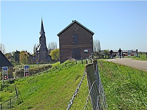 Een stenen gebouw op de dijk, op de achtergrond een kerktoren