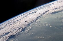 Fotografia em grande altitude onde se pode ver o verde da floresta em primeiro plano, com os rios serpenteando, e ao fundo nuvens de tempestade cobrindo o horizonte.