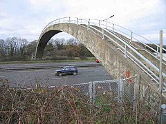 Photo d'une arche en béton avec des marches et des barrières de sécurité qui passe au-dessus d'une route à plusieurs voies sur laquelle circule une voiture