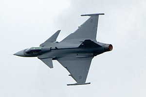 Grey fighter aircraft banking right, showing its top view, against a light blue sky