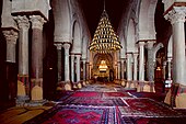 Photographie de la nef centrale de la salle de prière. Plus large et plus haute que les seize autres nefs, elle mène au mihrab. Elle est bordée, de part et d'autre, d'une double ligne d'arcades à colonnes géminées.