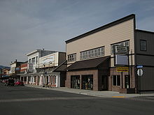 Ein kleines zweigeschossiges Gebäude mit einem Schild „Arlington Hardware & Lumber“ an der Straßenfront, das von ähnlichen Gebäuden mit anderen Geschäften begrenzt wird.