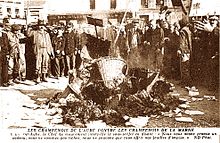 Photographie représentant un amas de diverses feuilles de papier et paniers d'osier devant un groupe d'hommes chantant et saluant du chapeau.