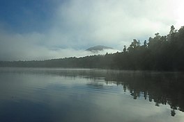 A still lake in the early morning with patchy mist, surrounded by forest