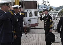 A colour photograph of naval personnel saluting each other on a sailing ship