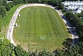 Die Luftaufnahme zeigt ein Betonoval mit überhöhten Kurven. In der Mitte ist ein Fußballplatz angelegt. Die Fahrbahn ist an vielen Stellen mit hellem Belag ausgebessert.