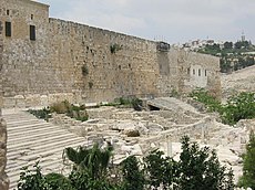 The long southern wall of Jerusalem's Temple Mount rises above two flights of stone steps between which are some low ruins