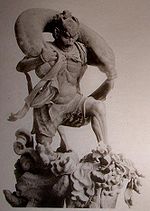 Fūjin. Three-quarter view of a statue. His left leg is bend as if climbing stairs et he is carrying a long bag-shaped object which goes from one shoulder to the other around the back of his head. Black and white photograph.