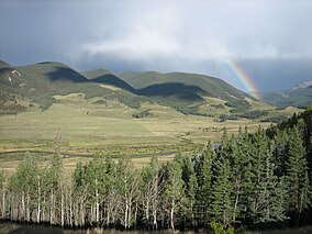 Landscape showing river flowing through green meadow surrounded by forested mountains