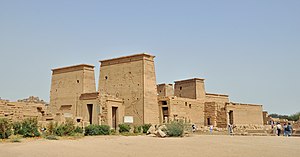 Stone building fronted by a tall gateway, a colonnade, and another gateway.