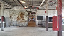 An open room with a wooden floor and a brick wall. The room's wooden ceiling is held up by wooden beams and wooden supports. A large sliding door is open, revealing similar rooms beyond.