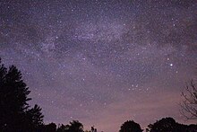 many stars in a dark purple sky, with silhouettes of a few trees on either side