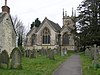 Gray three bay building with arched windows. Tower behind and gravestones in the foreground.