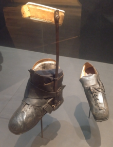 Photographie de deux chaussures prises de trois quarts, en cuir noir, la gauche étant de taille normale, la droite étant deux ou trois fois plus grande.