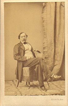 Photograph of Félix Milliet, posing cross-legged on a chair.