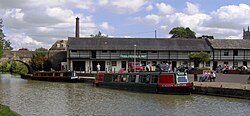 Water with two narrow boats and bridge. On the far side is a white coloured building displaying a banner which says Canal Museum and Shop.