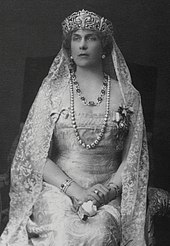 Portrait de trois-quarts d'une femme assise portant un diadème, un voile et un long collier de perles.