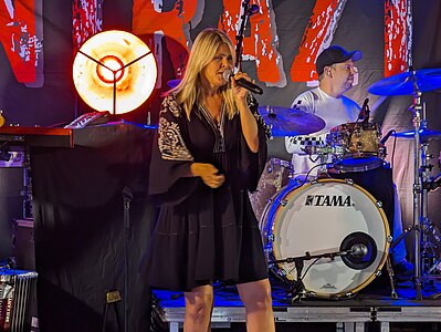 En sångerska med mikrofon i handen framför en trummis med sitt trumset på en scen.
