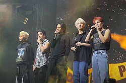 A photo of SB19 on stage, each holding a hand held microphone.