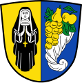 Gemeinde Nonnenhorn Gespalten von Gold und Blau; vorne eine schwarz gekleidete Nonne mit goldenem Rosenkranz, hinten ein silbernes Füllhorn mit goldener Weintraube, goldener Birne und goldenem Apfel mit grünen Blättern.