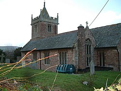 alt = Reddish stone church with square tower.