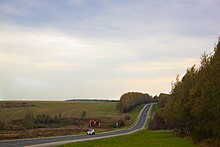 Photographie d'un paysage vallonné avec des champs et des haies d'arbres, avec une route passant à travers le paysage.