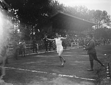 Photographie en noir et blanc d'un coureur à pied à l’arrivée d'une course dans un stade.