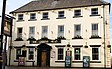 Front of a three-storey building, six windows across, with a large-framed wood door at ground level and a painted sign with the words "THE QUEENS HEAD"