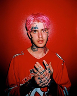 A man with tattoos on his hands and face, with pink hair stands against a red wall