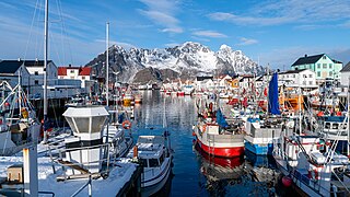 Foto eines Hafens mit vielen Booten und kleineren Schiffen, im Hintergrund schneebedeckte Berge