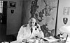 Black-and-white photo of a man wearing a white military uniform sitting at a desk, making a phone call.