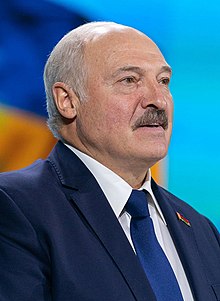 Lukashenko standing at a microphone, dressed in a suit