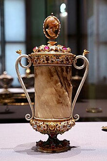 A goblet composed of narwhal tusk from Milan, Italy. The goblet is covered with jewels, has snake-shaped handles and a depiction of a woman at the top.