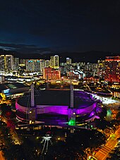 Aerial view of a lit-up convention centre at dusk, with high-rises as the backdrop.