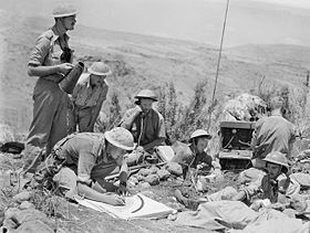 Seven men in military fatigues using radios and megaphones