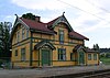 A wooden train station building in Dragestil, with a main color in dark orange and detailing in dark green