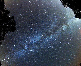 Black sky with a wide diagonal streak of bright blue stars, partially hidden by a silhouetted tree