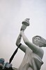 Plastic replica statue of a woman holding a torch with a black scarf tied around one arm