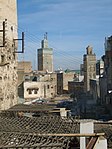 A picture of a sun-lit back alley with trash scattered across the area. Various buildings of varying architecture are clearly visible.