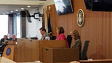 Three people seated on the dais of the county boardroom. From right to left, they are an assistant state's attorney, Conroy, and the Chief Deputy County Clerk.