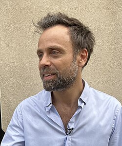 David Castello-Lopes souriant contre un mur au Festival d'Avignon.