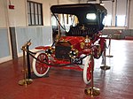 A red-colored, old-fashioned car with four seats and brass fittings