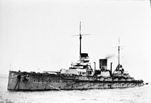 Una grande nave da guerra, immobile nel mare, la torretta anteriore è leggermente ruotata ed i cannoni puntano verso destra.