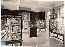 Photographie en noir et blanc d'une des salles du musée rénové, qui présente une muséographie soignée et aérée ; des céramiques sont exposées dans des vitrines.