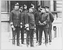 Eight men in front of a building's door at the center of a black and white photograph