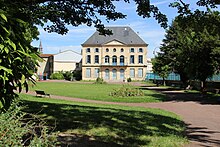 Pelouses et chemins avec au fond un bâtiment de pierre.