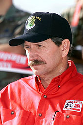 Dale Earnhardt wearing a black baseball cap with a military logo and a red shirt with the top button undone