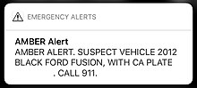 An amber alert on iOS. Text reads in all caps "Suspect vehicle 2012 black ford fusion, with ca plate [license plate removed]. Call 911.